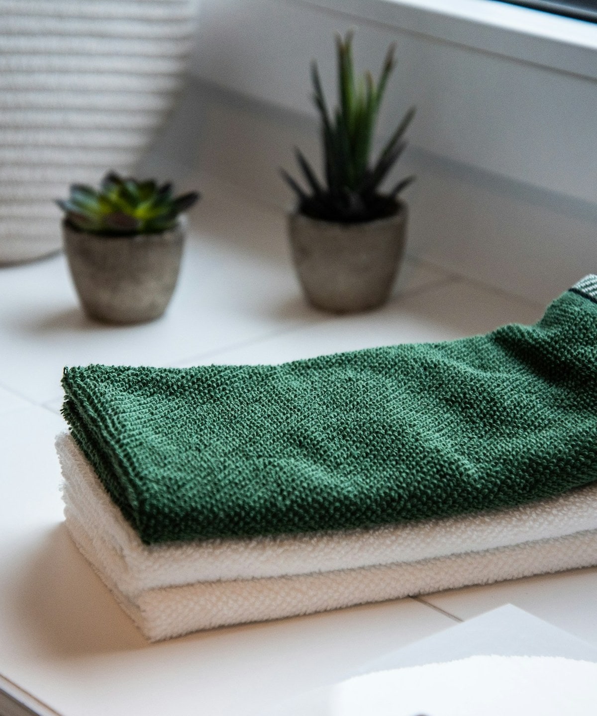 Neatly folded towels stacked beside potted plants on a bright windowsill